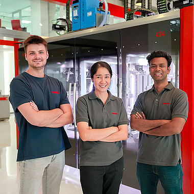 A group of three SOMIC APAC employees in front of a carton packaging machine in the bangkok showroom