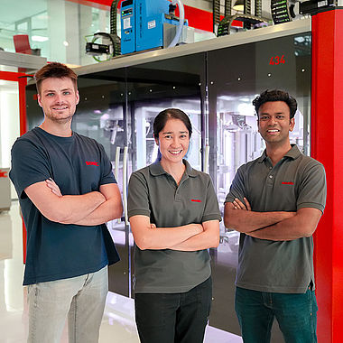 A group of three SOMIC APAC employees in front of a carton packaging machine in the bangkok showroom