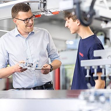 Ein SOMIC Auszubildender erhält eine Unterweisung von einem SOMIC Ausbilder an einer Kartonverpackungsmaschine.