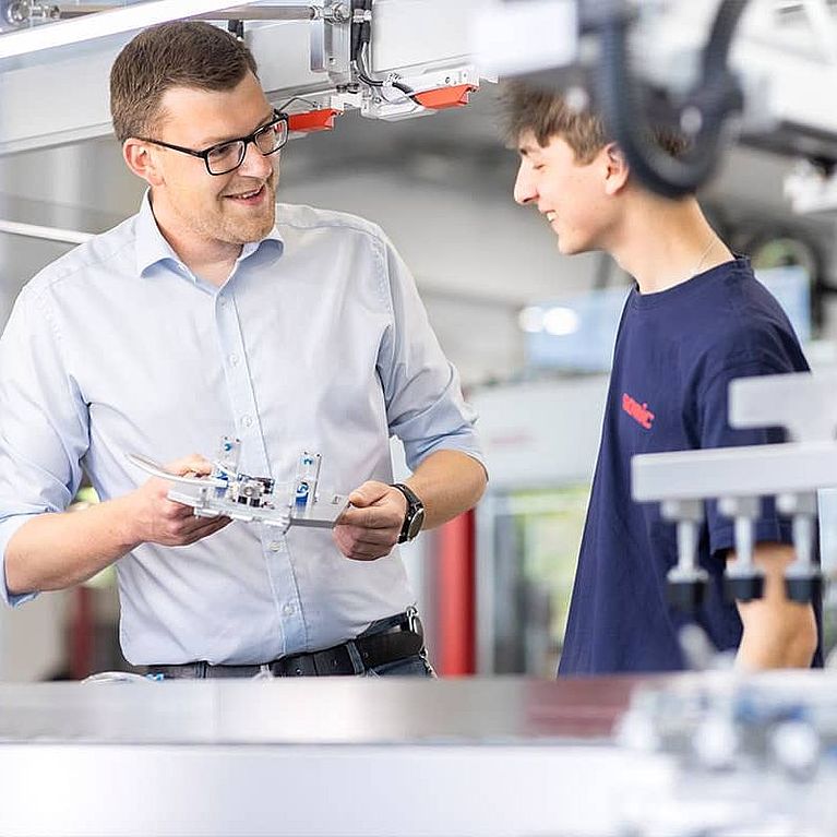 Ein SOMIC Auszubildender erhält eine Unterweisung von einem SOMIC Ausbilder an einer Kartonverpackungsmaschine.