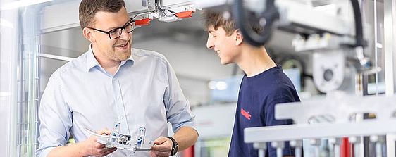 Ein SOMIC Auszubildender erhält eine Unterweisung von einem SOMIC Ausbilder an einer Kartonverpackungsmaschine.