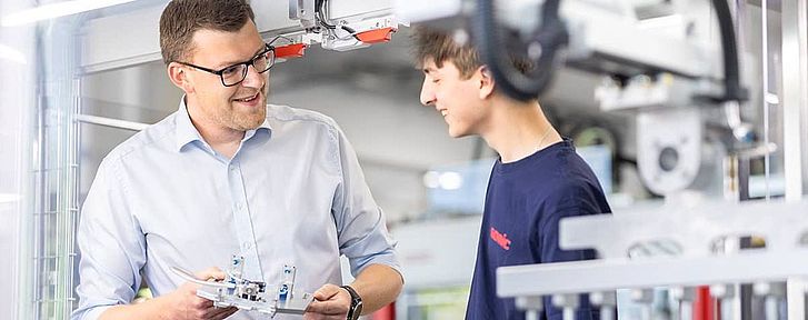 Ein SOMIC Auszubildender erhält eine Unterweisung von einem SOMIC Ausbilder an einer Kartonverpackungsmaschine.