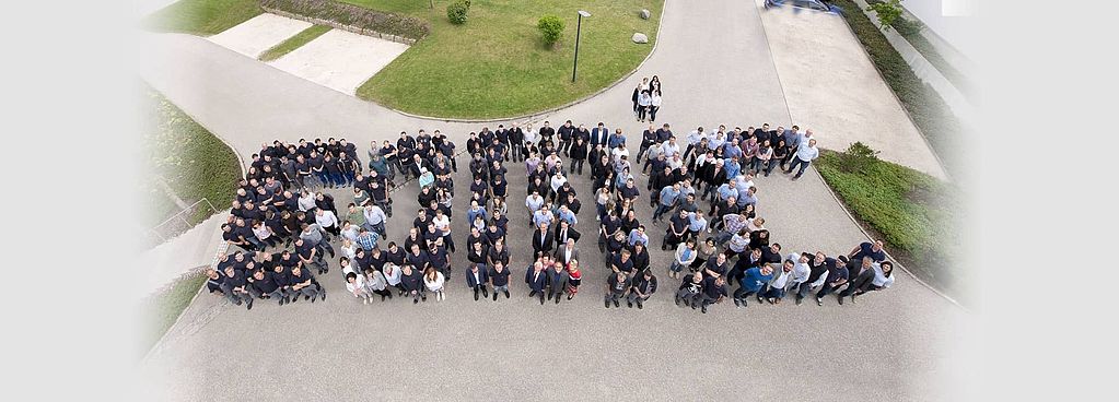 Das Headerbild zeigt SOMIC Mitarbeitende aufgestellt zu einem Gruppenbild. Die aufgestellten Personen ergeben so das Wort "SOMIC"