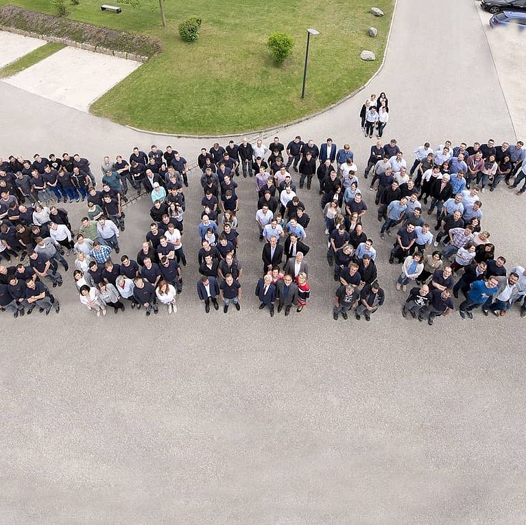 Das Headerbild zeigt SOMIC Mitarbeitende aufgestellt zu einem Gruppenbild. Die aufgestellten Personen ergeben so das Wort "SOMIC"