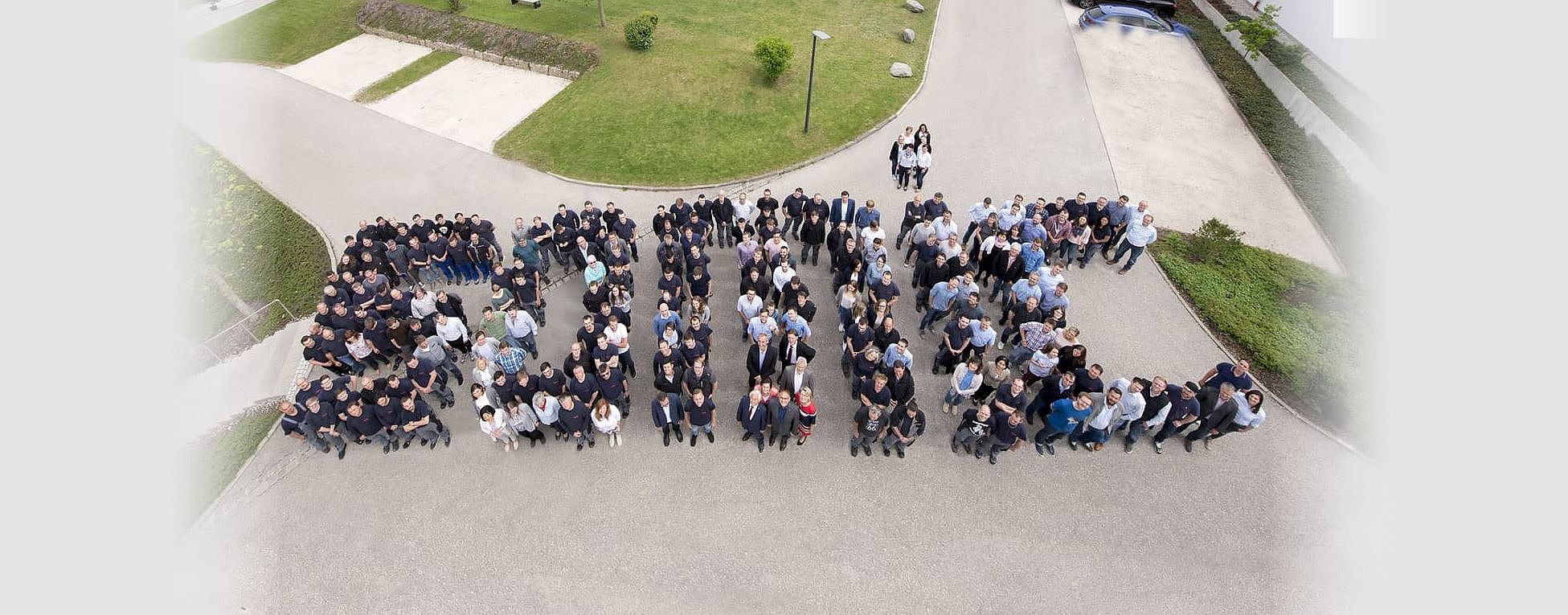 Das Headerbild zeigt SOMIC Mitarbeitende aufgestellt zu einem Gruppenbild. Die aufgestellten Personen ergeben so das Wort "SOMIC"