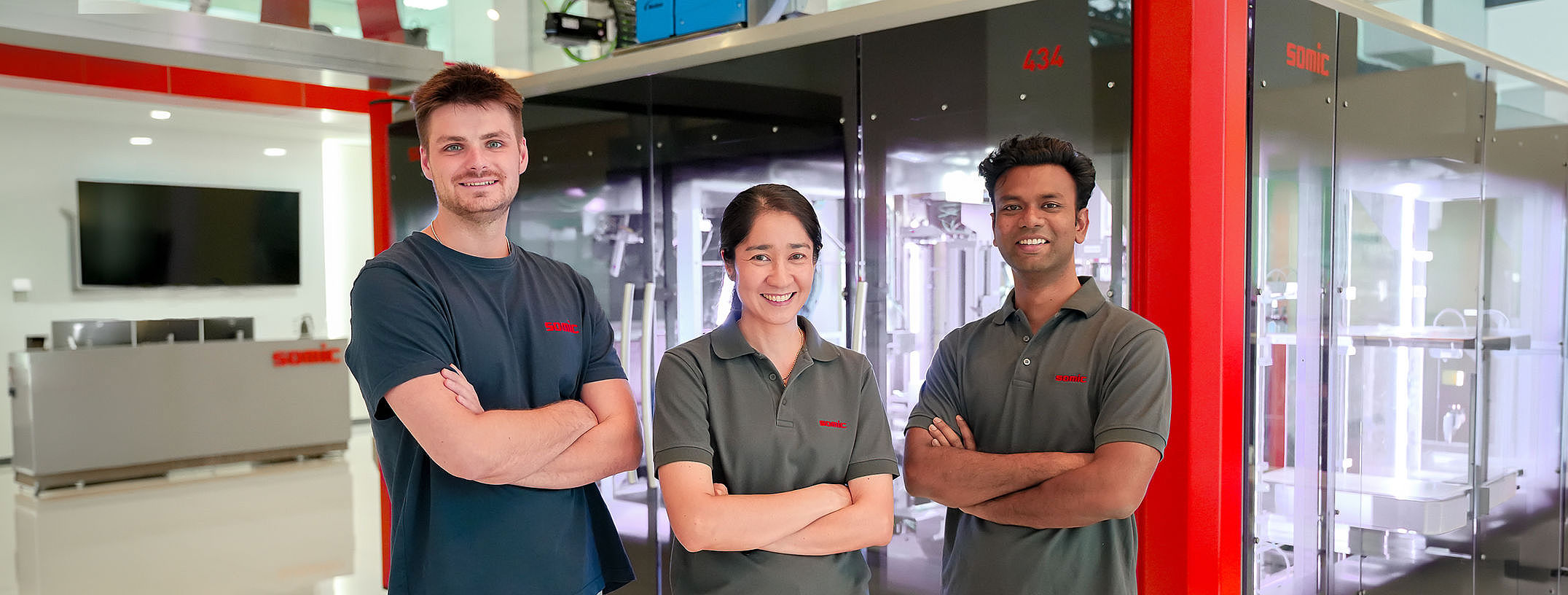A group of SOMIC APAC employees in front of a SOMIC carton packaging machine in the Bangkok office