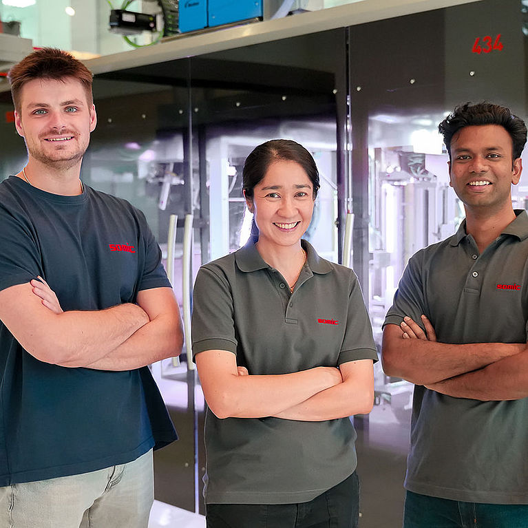 A group of SOMIC APAC employees in front of a SOMIC carton packaging machine in the Bangkok office